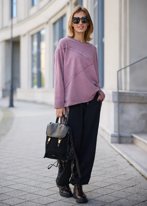 Bluza damska oversize w odcieniu brudnego różu z efektem sprania, z okrągłym dekoltem, obniżoną linią ramion, długimi rękawami, asymetrycznymi przeszyciami o postrzępionych krawędziach oraz naszywaną kieszenią z przodu.