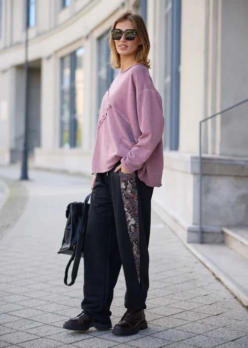 Bluza damska oversize w odcieniu brudnego różu z efektem sprania, z okrągłym dekoltem, obniżoną linią ramion, długimi rękawami, asymetrycznymi przeszyciami o postrzępionych krawędziach oraz naszywaną kieszenią z przodu.