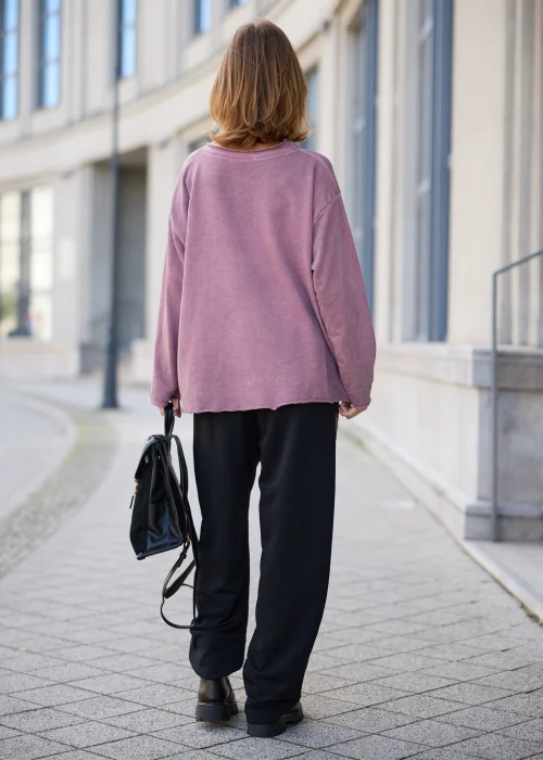 Bluza damska oversize w odcieniu brudnego różu z efektem sprania, z okrągłym dekoltem, obniżoną linią ramion, długimi rękawami, asymetrycznymi przeszyciami o postrzępionych krawędziach oraz naszywaną kieszenią z przodu.