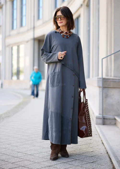 Sukienka damska maxi w kolorze grafitowoszarym, o mocno oversize’owym fasonie, z długimi rękawami, okrągłym dekoltem, asymetryczną warstwą materiału, pionowym rzędem guzików i dużą naszywaną kieszenią.