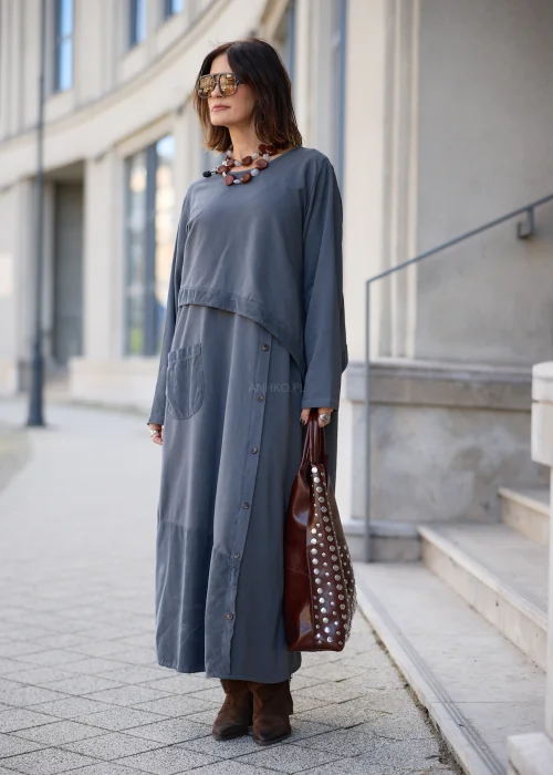 Sukienka damska maxi w kolorze grafitowoszarym, o mocno oversize’owym fasonie, z długimi rękawami, okrągłym dekoltem, asymetryczną warstwą materiału, pionowym rzędem guzików i dużą naszywaną kieszenią.