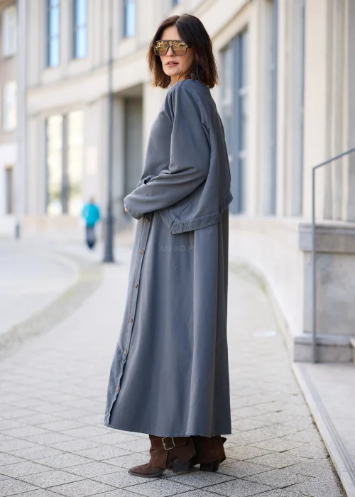 Sukienka damska maxi w kolorze grafitowoszarym, o mocno oversize’owym fasonie, z długimi rękawami, okrągłym dekoltem, asymetryczną warstwą materiału, pionowym rzędem guzików i dużą naszywaną kieszenią.