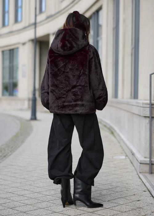 Burgundowe futro damskie oversize z kapturem, miękkim sztucznym futerkiem i ozdobnymi broszkami przy zapięciu oraz rękawach.