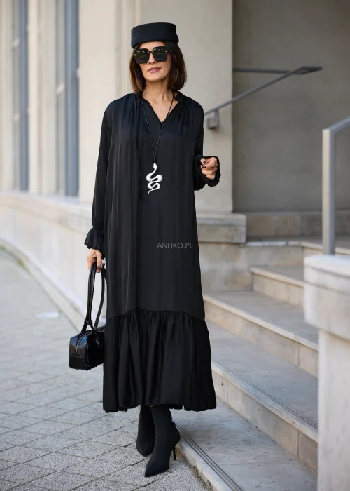 Sukienka damska maxi w kolorze czarnym, o luźnym fasonie oversize, z długimi rękawami zakończonymi marszczonymi mankietami, dekoltem w serek z wiązaniem oraz szeroką, marszczoną falbaną u dołu.