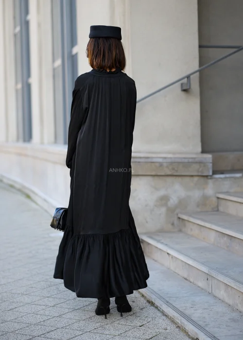 Sukienka damska maxi w kolorze czarnym, o luźnym fasonie oversize, z długimi rękawami zakończonymi marszczonymi mankietami, dekoltem w serek z wiązaniem oraz szeroką, marszczoną falbaną u dołu.