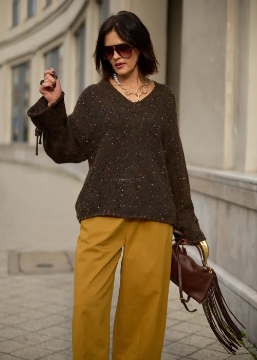 Sweter damski oversize z miękkiej, lekko puszystej dzianiny w kolorze ciemnego czekoladowego brązu, ozdobiony drobnymi, wielokolorowymi akcentami przypominającymi konfetti, z dekoltem w serek, obniżoną linią ramion