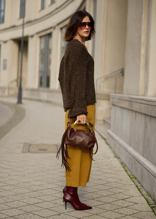 Sweter damski oversize z miękkiej, lekko puszystej dzianiny w kolorze ciemnego czekoladowego brązu, ozdobiony drobnymi, wielokolorowymi akcentami przypominającymi konfetti, z dekoltem w serek, obniżoną linią ramion