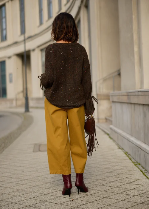 Sweter damski oversize z miękkiej, lekko puszystej dzianiny w kolorze ciemnego czekoladowego brązu, ozdobiony drobnymi, wielokolorowymi akcentami przypominającymi konfetti, z dekoltem w serek, obniżoną linią ramion