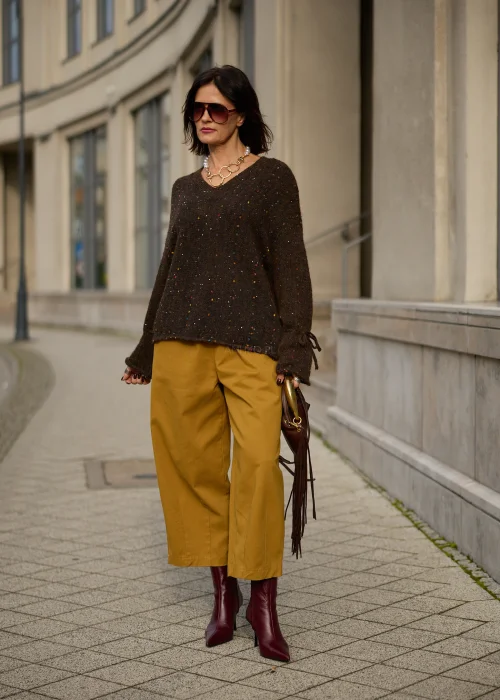 Sweter damski oversize z miękkiej, lekko puszystej dzianiny w kolorze ciemnego czekoladowego brązu, ozdobiony drobnymi, wielokolorowymi akcentami przypominającymi konfetti, z dekoltem w serek, obniżoną linią ramion