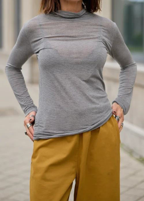 Bluzka damska dzianinowa w kolorze jasnoszarego melanżu, o lekko dopasowanym fasonie, z długimi, wąskimi rękawami, delikatnie marszczonym półgolfem oraz cienką, subtelnie transparentną dzianiną o miękkiej, delikatnej strukturze.
