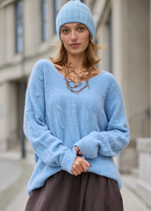 Sweter damski oversize z miękkiej, puszystej dzianiny w kolorze jasnego błękitu, z szerokim dekoltem w serek, obniżoną linią ramion, długimi rękawami zakończonymi szerokimi prążkowanymi mankietami