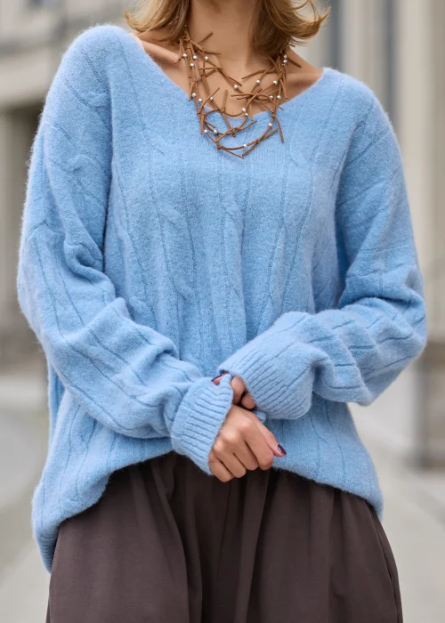 Sweter damski oversize z miękkiej, puszystej dzianiny w kolorze jasnego błękitu, z szerokim dekoltem w serek, obniżoną linią ramion, długimi rękawami zakończonymi szerokimi prążkowanymi mankietami
