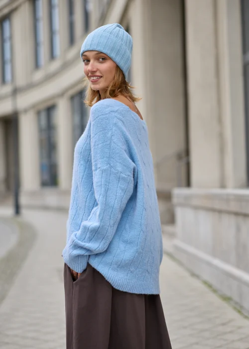 Sweter damski oversize z miękkiej, puszystej dzianiny w kolorze jasnego błękitu, z szerokim dekoltem w serek, obniżoną linią ramion, długimi rękawami zakończonymi szerokimi prążkowanymi mankietami