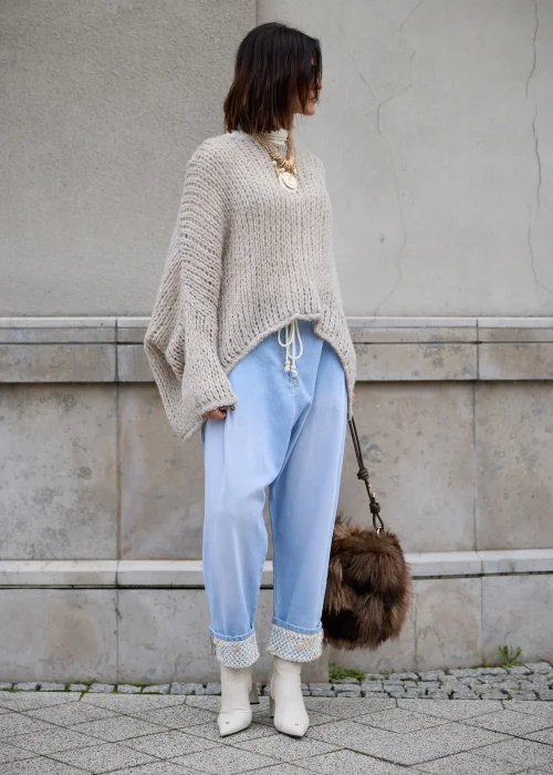 Sweter damski oversize z grubej, puszystej dzianiny o luźnym, ażurowym splocie w kolorze jasnego beżu, z okrągłym dekoltem, obniżoną linią ramion, długimi szerokimi rękawami oraz asymetrycznym, łukowato wyciętym dołem.