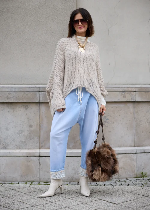 Sweter damski oversize z grubej, puszystej dzianiny o luźnym, ażurowym splocie w kolorze jasnego beżu, z okrągłym dekoltem, obniżoną linią ramion, długimi szerokimi rękawami oraz asymetrycznym, łukowato wyciętym dołem.