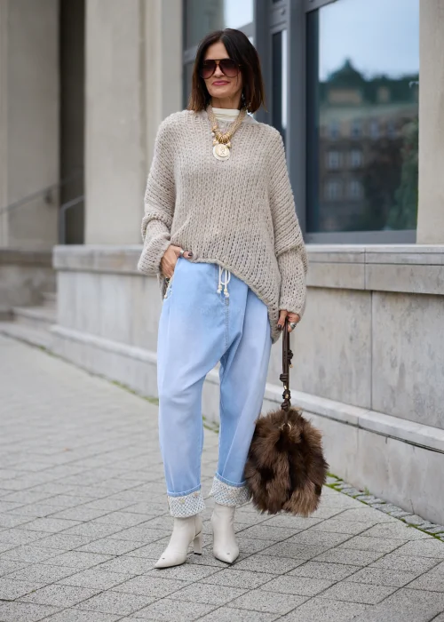 Sweter damski oversize z grubej, puszystej dzianiny o luźnym, ażurowym splocie w kolorze jasnego beżu, z okrągłym dekoltem, obniżoną linią ramion, długimi szerokimi rękawami oraz asymetrycznym, łukowato wyciętym dołem.