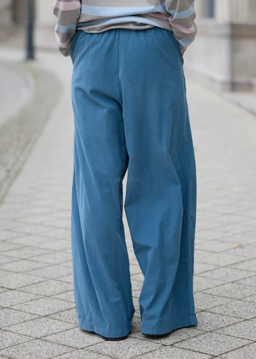 Niebieskie spodnie damskie oversize z bardzo szerokimi, długimi nogawkami, elastycznym pasem z wiązaniem na troczki, bocznymi kieszeniami i luźnym, swobodnym fasonem.