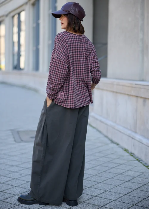 Bluzka damska oversize w drobną kratkę w odcieniach przygaszonego różu, fioletu i grafitu, z okrągłym dekoltem, obniżoną linią ramion, długimi rękawami, surowym wykończeniem brzegów oraz luźnym fasonem.
