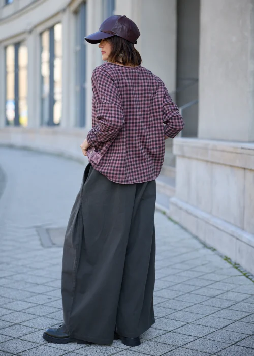 Bluzka damska oversize w drobną kratkę w odcieniach przygaszonego różu, fioletu i grafitu, z okrągłym dekoltem, obniżoną linią ramion, długimi rękawami, surowym wykończeniem brzegów oraz luźnym fasonem.