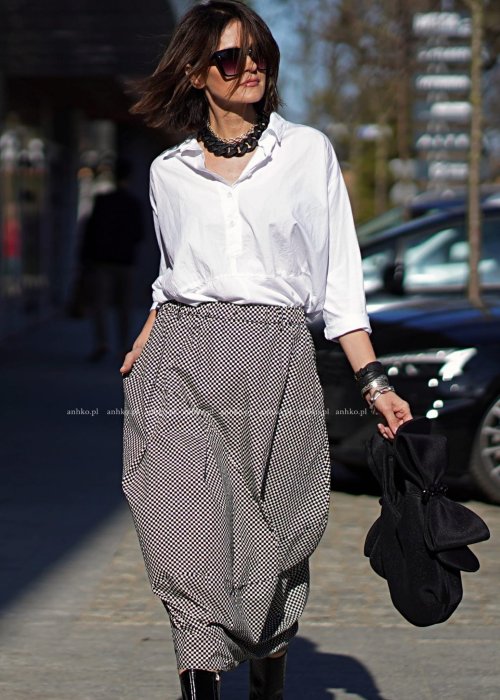 Biała koszula damska oversize z kołnierzykiem i przeszyciem poniżej biustu, zestawiona z czarno-białą spódnicą w geometryczny wzór w miejskiej stylizacji.