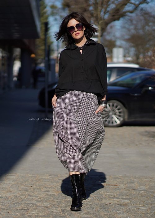 Czarna koszula damska oversize z kołnierzykiem i przeszyciem poniżej biustu, zestawiona z czarno-białą spódnicą w geometryczny wzór w miejskiej stylizacji.