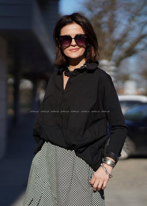 Czarna koszula damska oversize z kołnierzykiem i przeszyciem poniżej biustu, zestawiona z czarno-białą spódnicą w geometryczny wzór w miejskiej stylizacji.