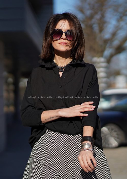 Czarna koszula damska oversize z kołnierzykiem i przeszyciem poniżej biustu, zestawiona z czarno-białą spódnicą w geometryczny wzór w miejskiej stylizacji.