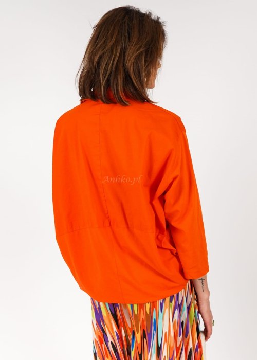 Pomarańczowa koszula damska oversize z bawełny zapinana na guziki, z przeszyciem poniżej biustu. Model pokazany w stylizacji z kolorową, wzorzystą spódnicą.