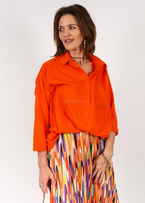 Pomarańczowa koszula damska oversize z bawełny zapinana na guziki, z przeszyciem poniżej biustu. Model pokazany w stylizacji z kolorową, wzorzystą spódnicą.