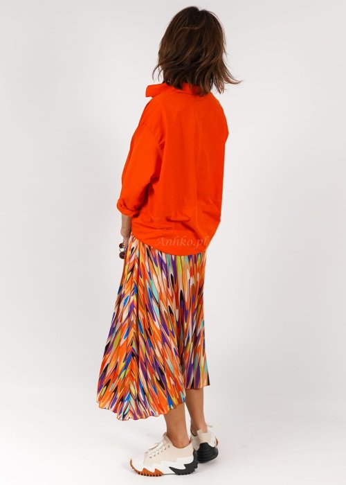 Pomarańczowa koszula damska oversize z bawełny zapinana na guziki, z przeszyciem poniżej biustu. Model pokazany w stylizacji z kolorową, wzorzystą spódnicą.