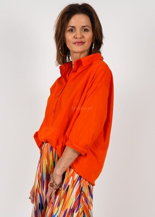 Pomarańczowa koszula damska oversize z bawełny zapinana na guziki, z przeszyciem poniżej biustu. Model pokazany w stylizacji z kolorową, wzorzystą spódnicą.