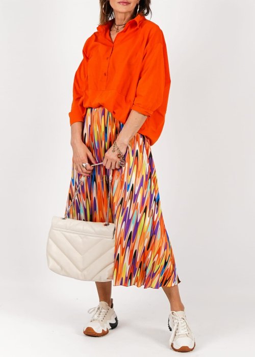 Pomarańczowa koszula damska oversize z bawełny zapinana na guziki, z przeszyciem poniżej biustu. Model pokazany w stylizacji z kolorową, wzorzystą spódnicą.