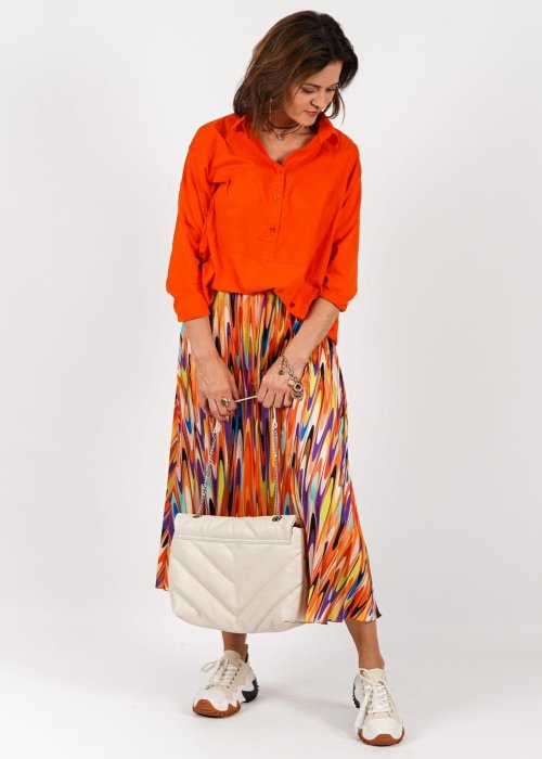 Pomarańczowa koszula damska oversize z bawełny zapinana na guziki, z przeszyciem poniżej biustu. Model pokazany w stylizacji z kolorową, wzorzystą spódnicą.