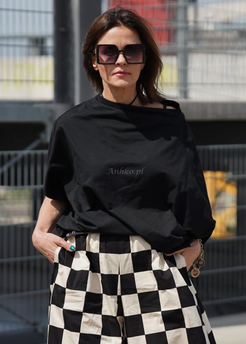 Czarna bluzka oversize z rękawem typu nietoperz i asymetrycznym dołem, stylizowana z szerokimi spodniami w kratę w miejskim looku.