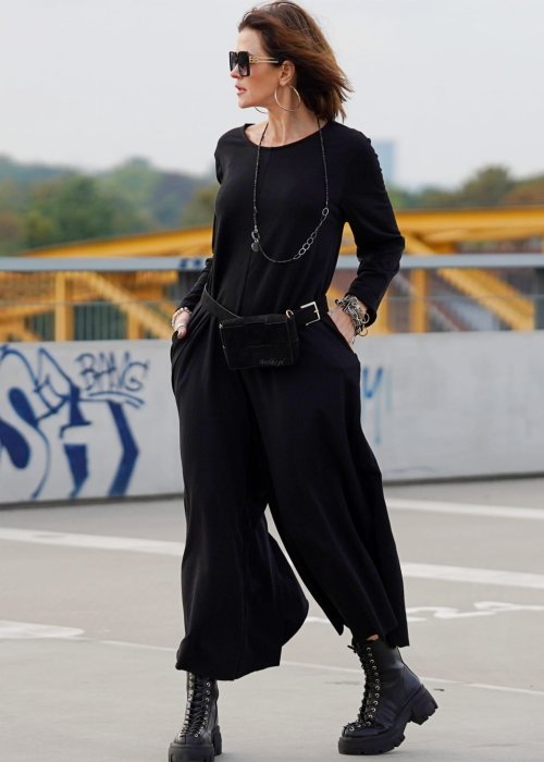 Czarny kombinezon damski z długim rękawem i bardzo szeroką nogawką, luźny fason w stylizacji z ciężkimi botkami na platformie.