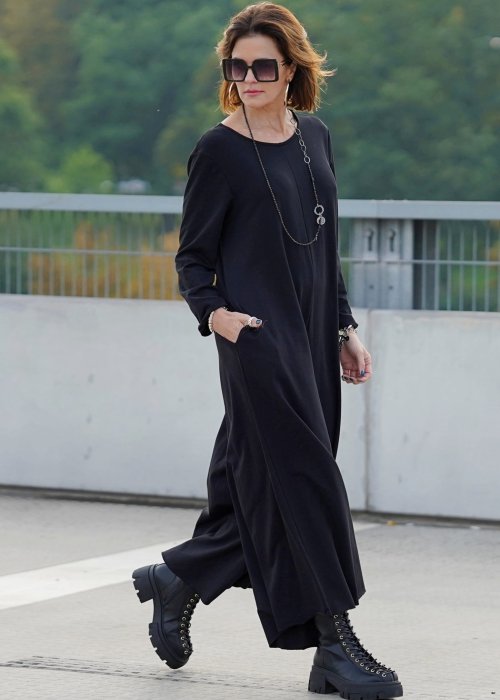 Czarny kombinezon damski z długim rękawem i bardzo szeroką nogawką, luźny fason w stylizacji z ciężkimi botkami na platformie.