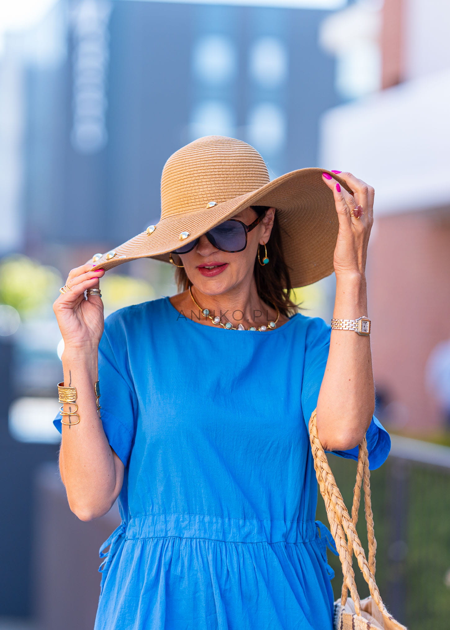 Stylowa kobieta w camelowym kapeluszu z perłami i niebieskiej sukience