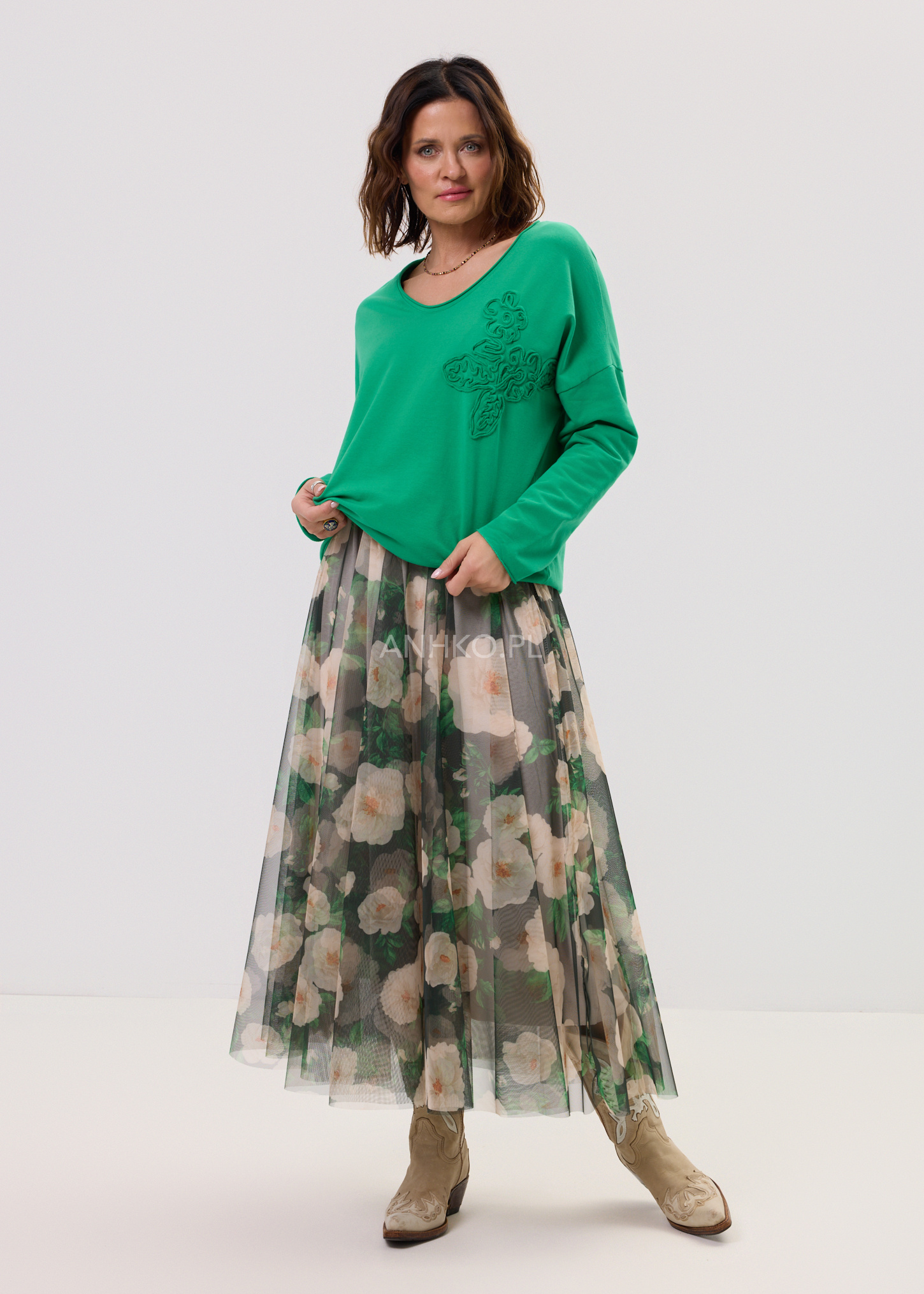 Kobieta w zielonej bluzce damskiej i tiulowej spódnicy midi w kwiatowy wzór