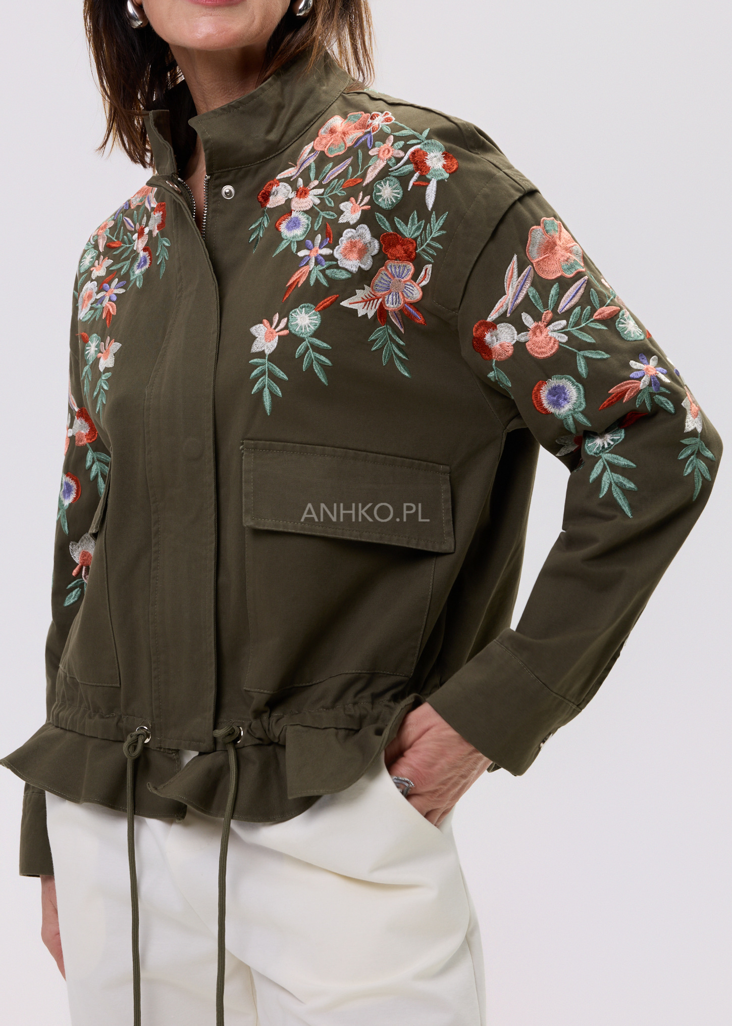 Damska kurtka khaki zapinana na zamek z haftowanymi kwiatami na ramionach i rękawach, model z kieszeniami i regulacją w pasie, elegancka stylizacja.